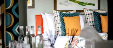 A hotel room with a bed featuring patterned pillows, a bedside table with bottles, glasses, and a red object.