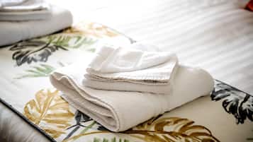 A neatly folded stack of white towels on a bed with a floral-patterned bedspread.