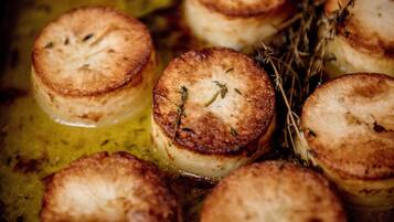 A close-up of several round, golden-brown pastries with herbs, likely baked in an oil bath.