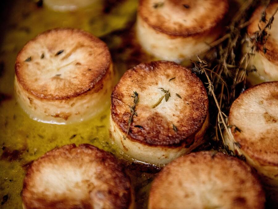 A close-up of several round, golden-brown pastries with herbs, likely baked in an oil bath.