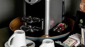 Une machine à café avec deux tasses et leurs soucoupes, un plateau de dosettes de café et un certificat encadré posé sur une table.