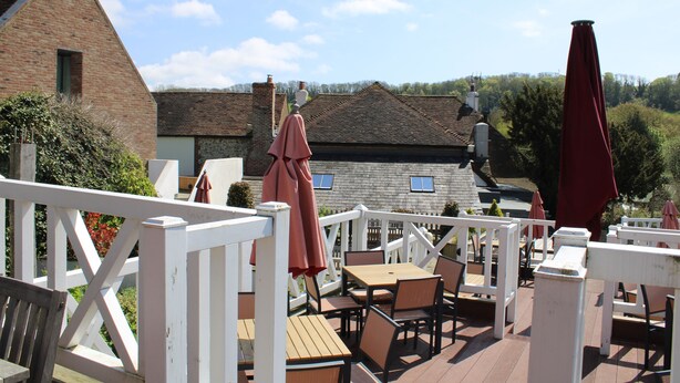 A wooden deck with outdoor seating and umbrellas, overlooking a brick building and trees. - Marquis Of Granby (Dover)