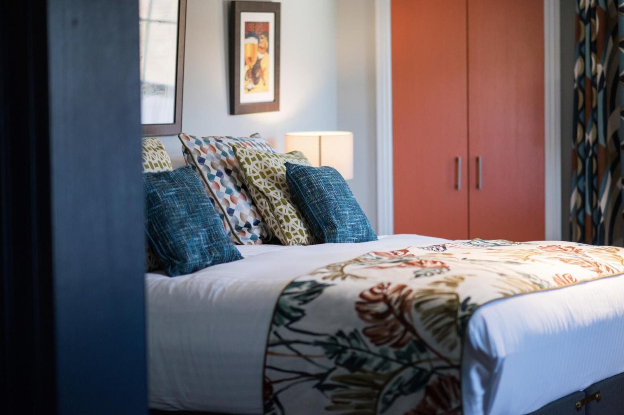Une chambre à coucher avec un lit, des oreillers, une table de chevet, une lampe et une armoire.