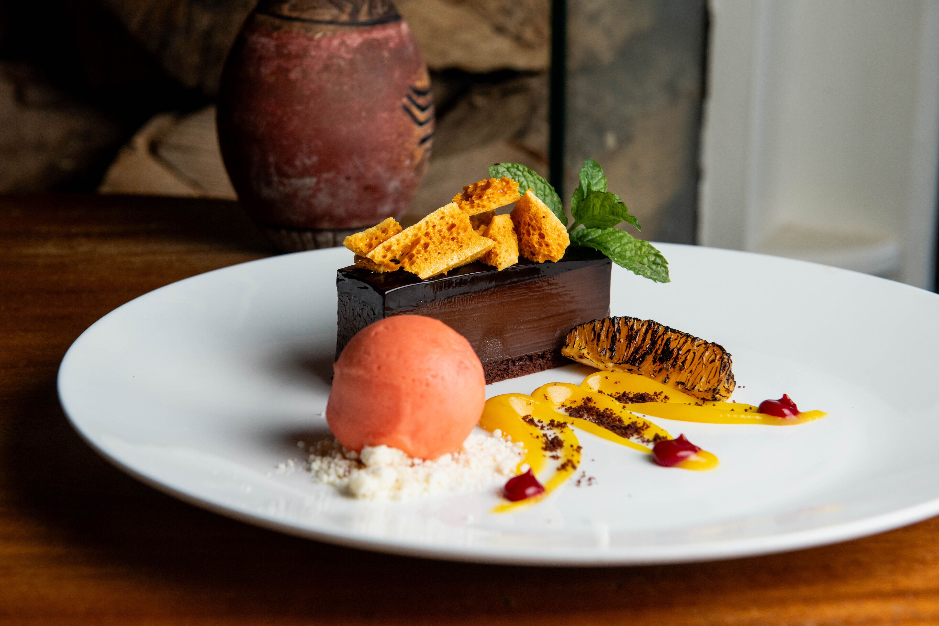 Ein Desserteller mit einer Kugel Eis, einem Kuchenstück und etwas Obst auf einem weißen Teller.
