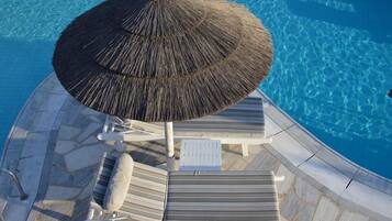 A poolside area with lounge chairs, a thatched umbrella, and a stone tiled deck.