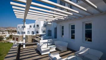 A white outdoor seating area with white furniture, a pergola, and a view of white buildings in the background.