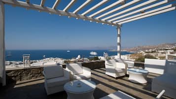 Una terrazza con arredi bianchi, una pergola e vista sul mare e sugli edifici in lontananza.