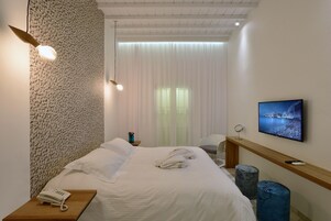 A hotel room with a bed, a bedside phone, a TV, and a large window with curtains.