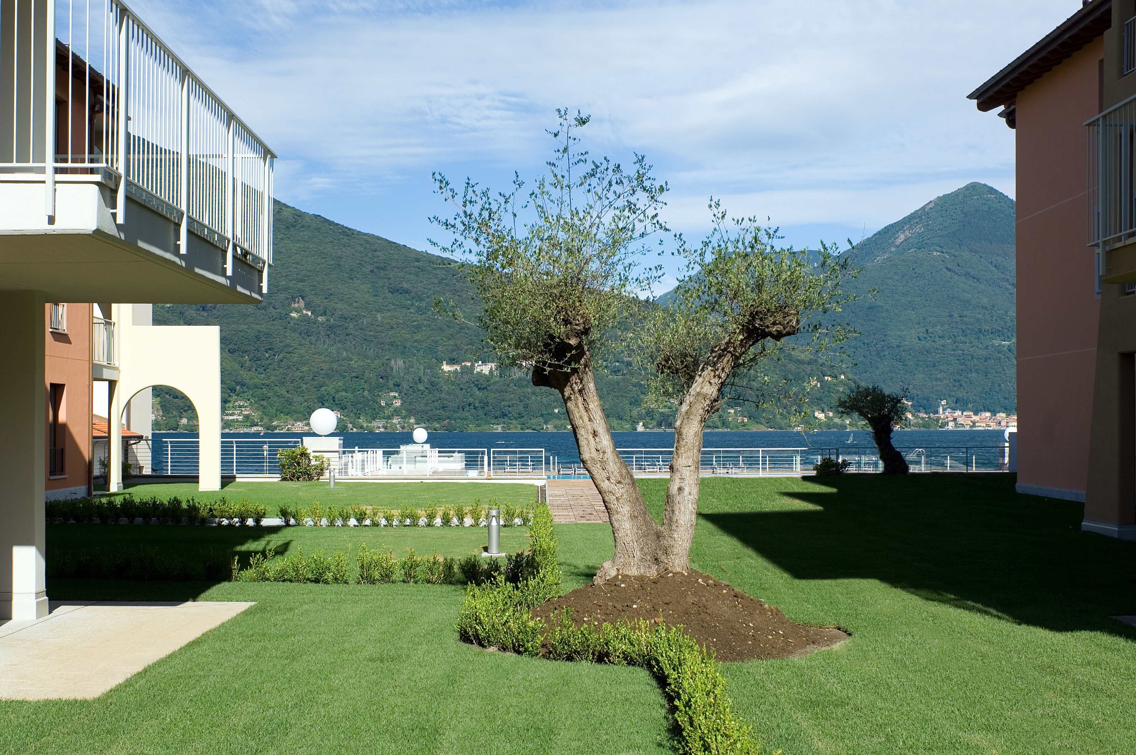 Un jardin aménagé avec un arbre, un bâtiment doté d’un balcon et une montagne en arrière-plan.