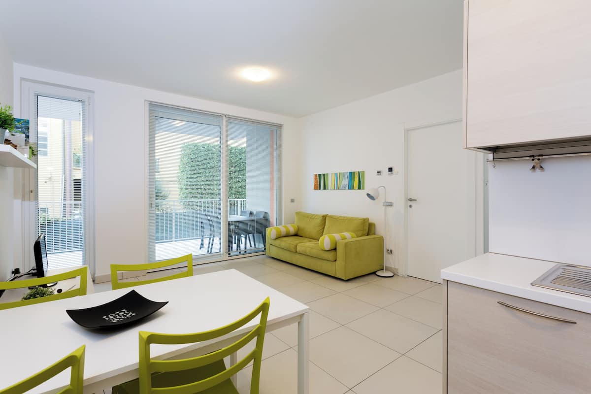 A modern, well-lit room with a dining table, chairs, a sofa, and a kitchenette.
