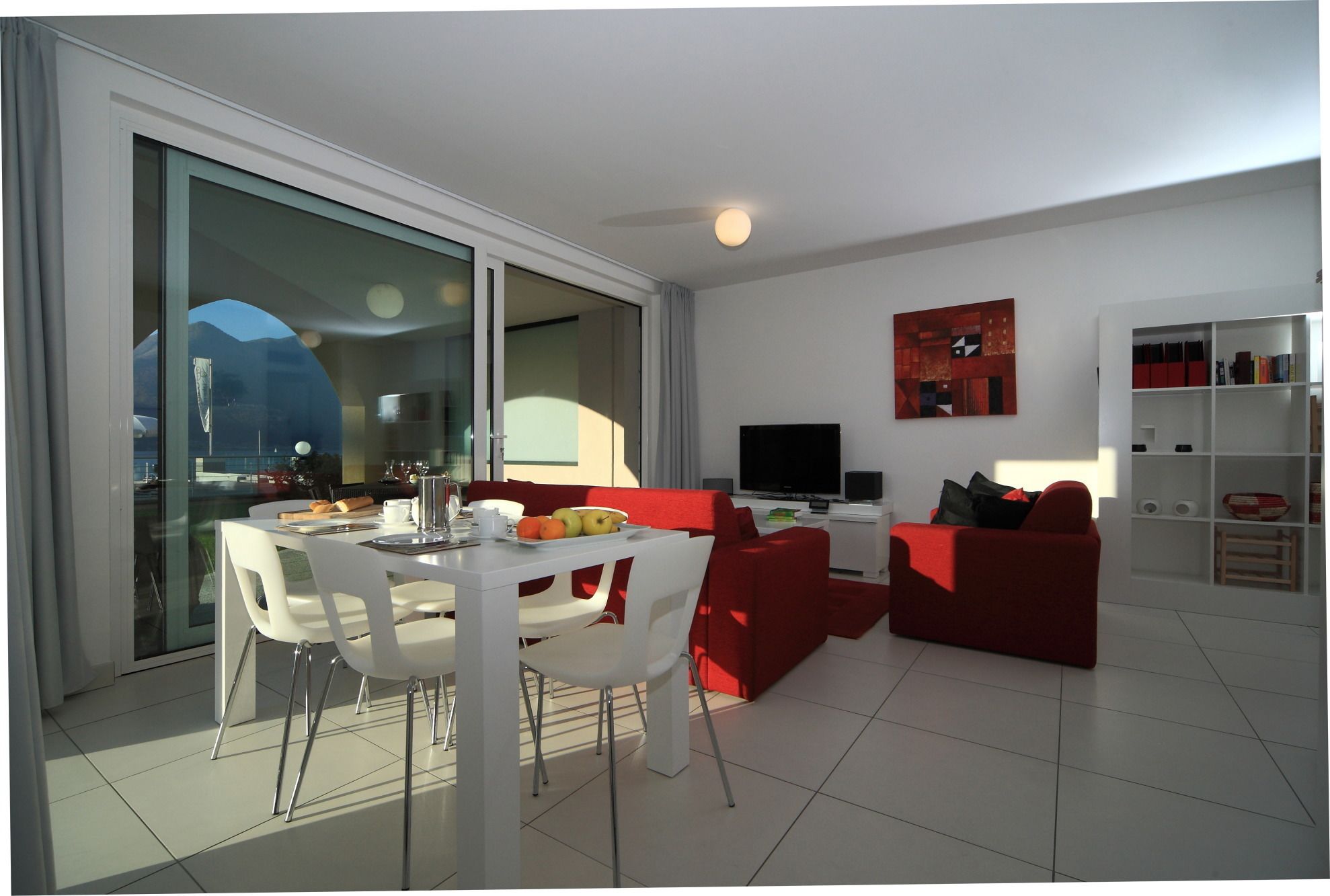 A modern living room with a dining area, a flat-screen TV, and a bookshelf.