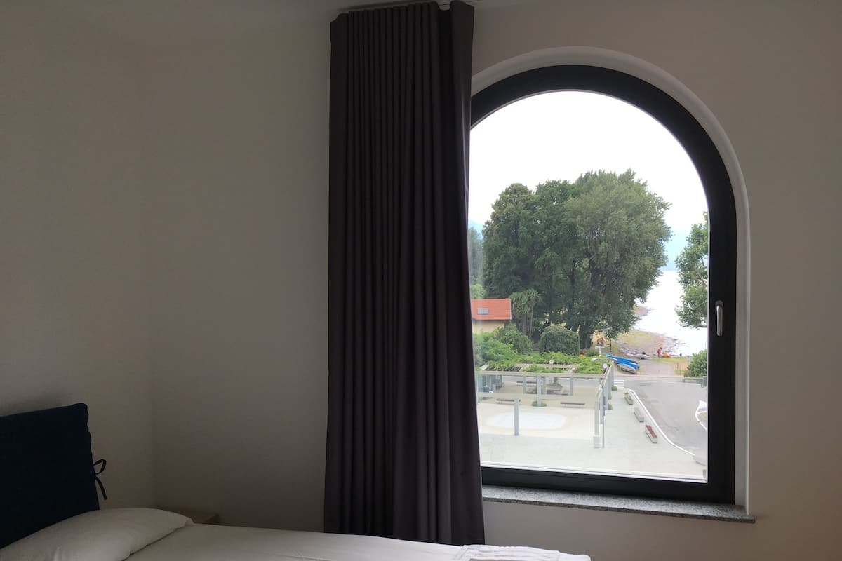 A hotel room with a bed, a window with a view of a street and trees, and a curtain.