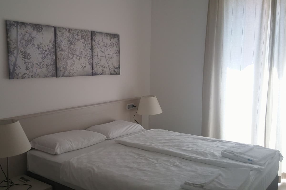 A hotel room with a large bed, two bedside lamps, and a wall-mounted artwork.