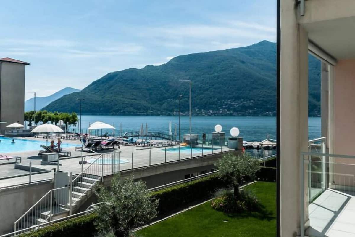 A pool area with lounge chairs and umbrellas, a staircase, and a view of a lake with mountains in the background.