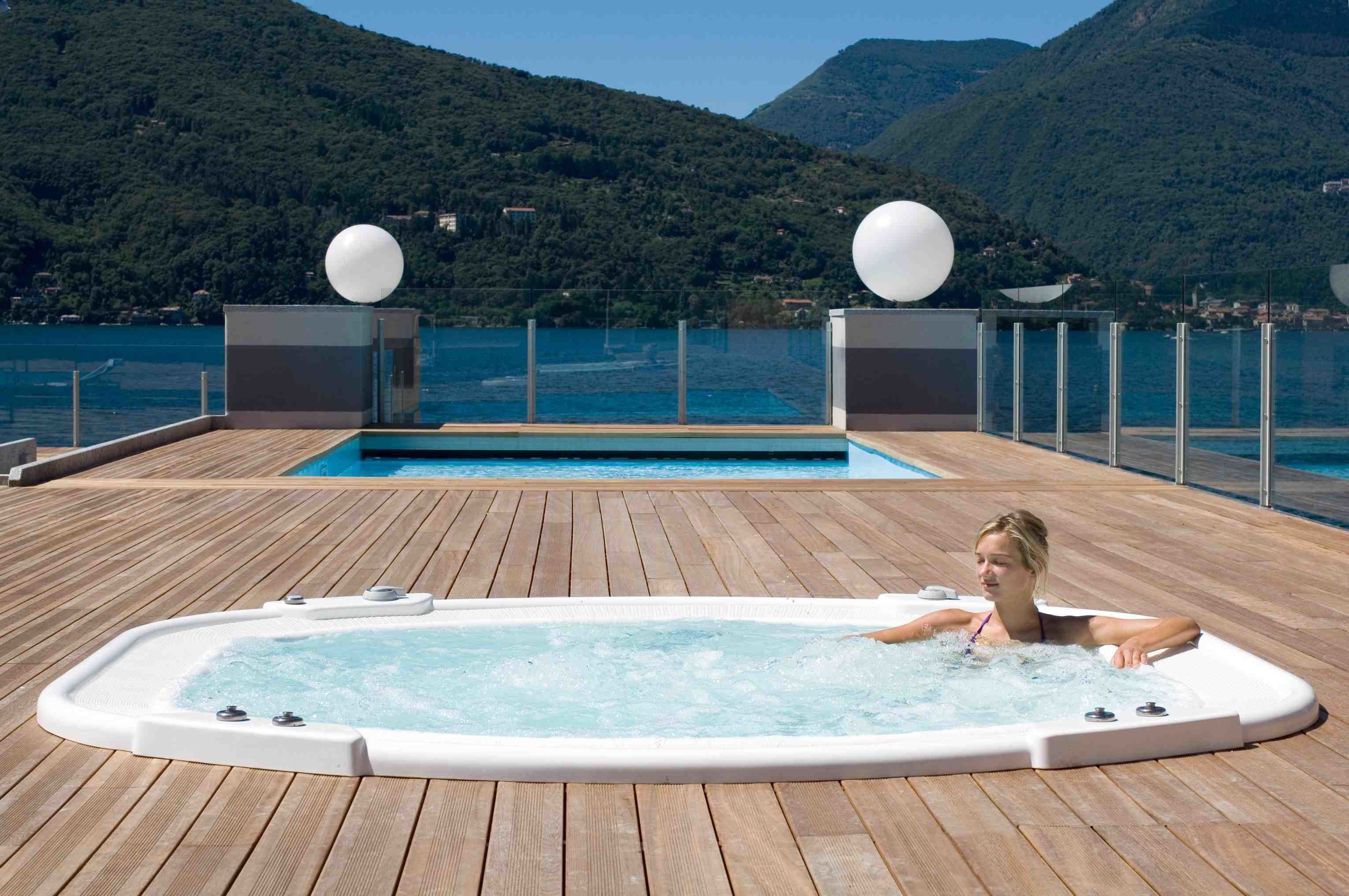 A wooden deck with a hot tub, a pool, and a mountain backdrop.