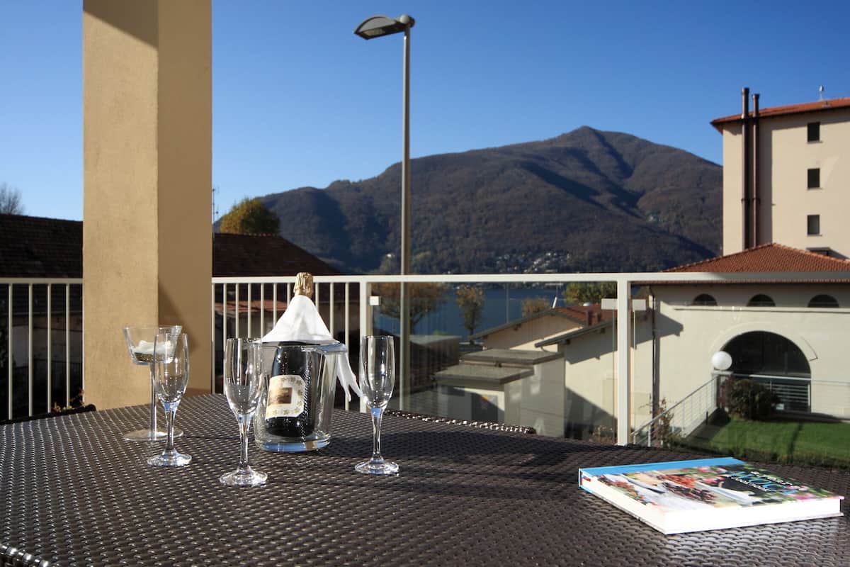 A table with wine glasses and a bottle, overlooking a mountain and buildings.