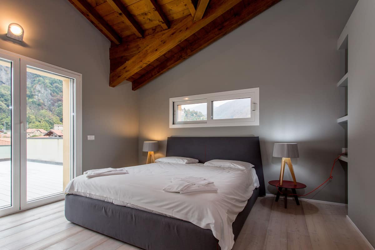 A bedroom with a large bed, two bedside lamps, a window, and a wooden ceiling.