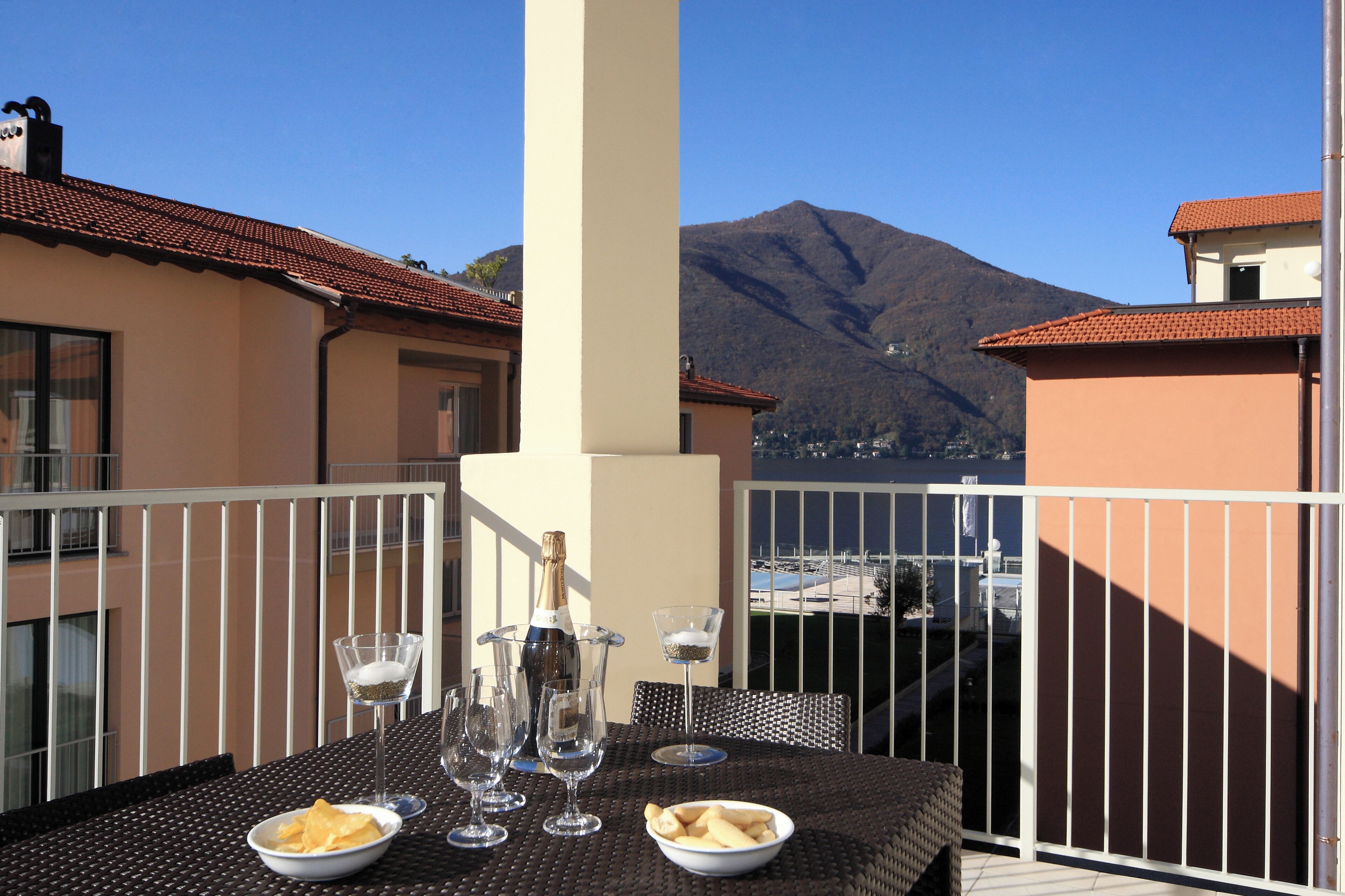 Un balcon avec une table dressée pour un repas, comprenant une bouteille de champagne, des verres et un bol de chips.