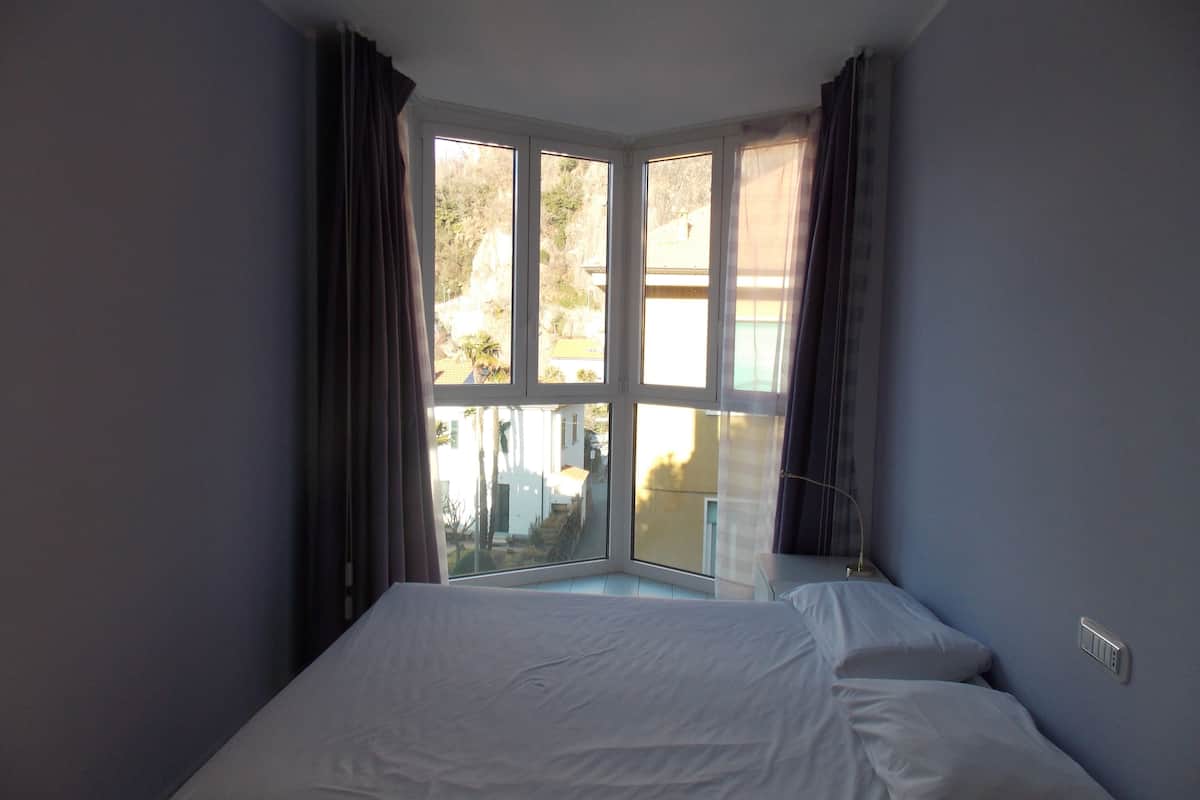A bedroom with a large window, a bed, and a bedside table.
