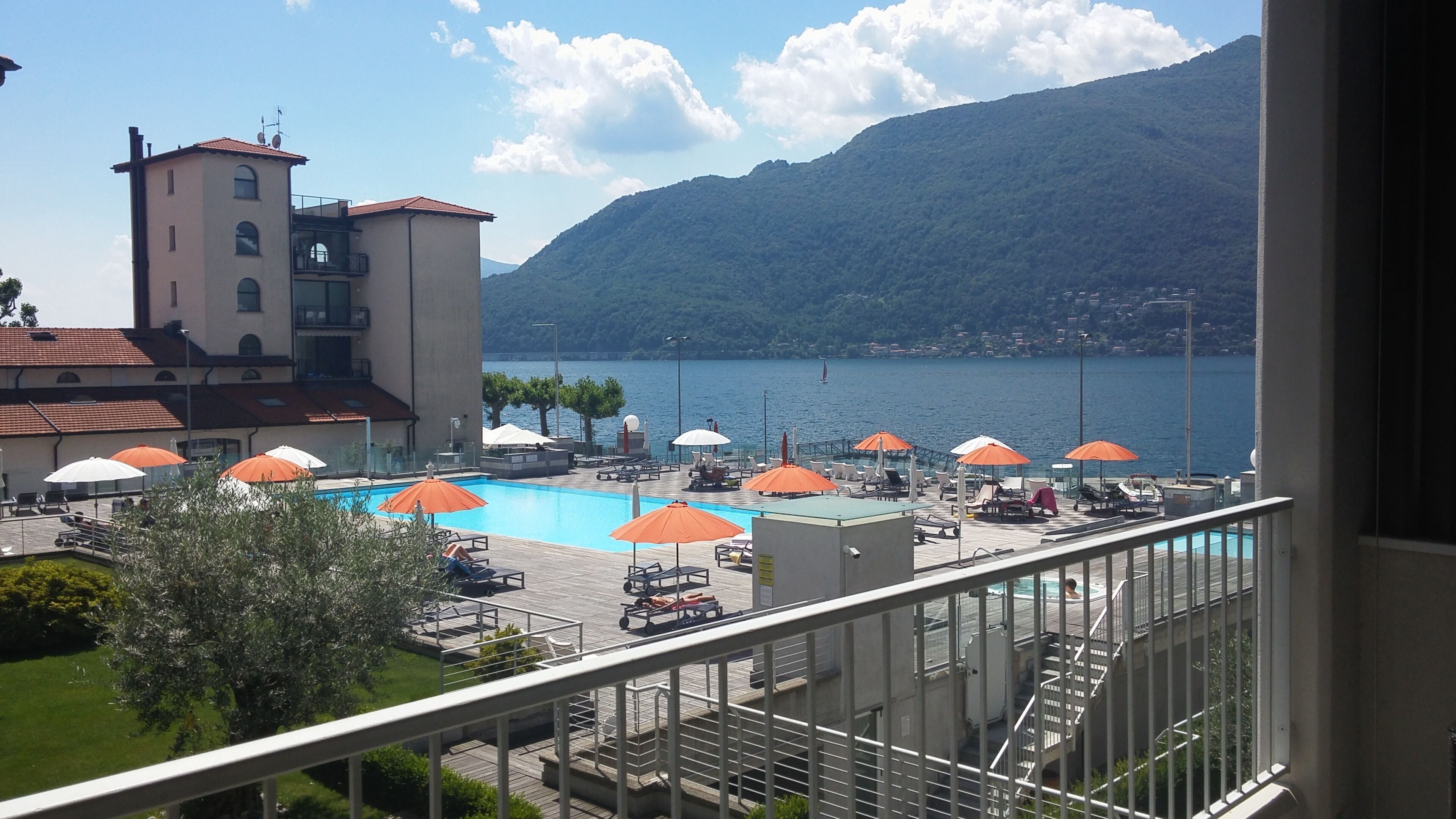 Un espace piscine équipé de parasols, de chaises longues et offrant une vue sur un lac et des montagnes.
