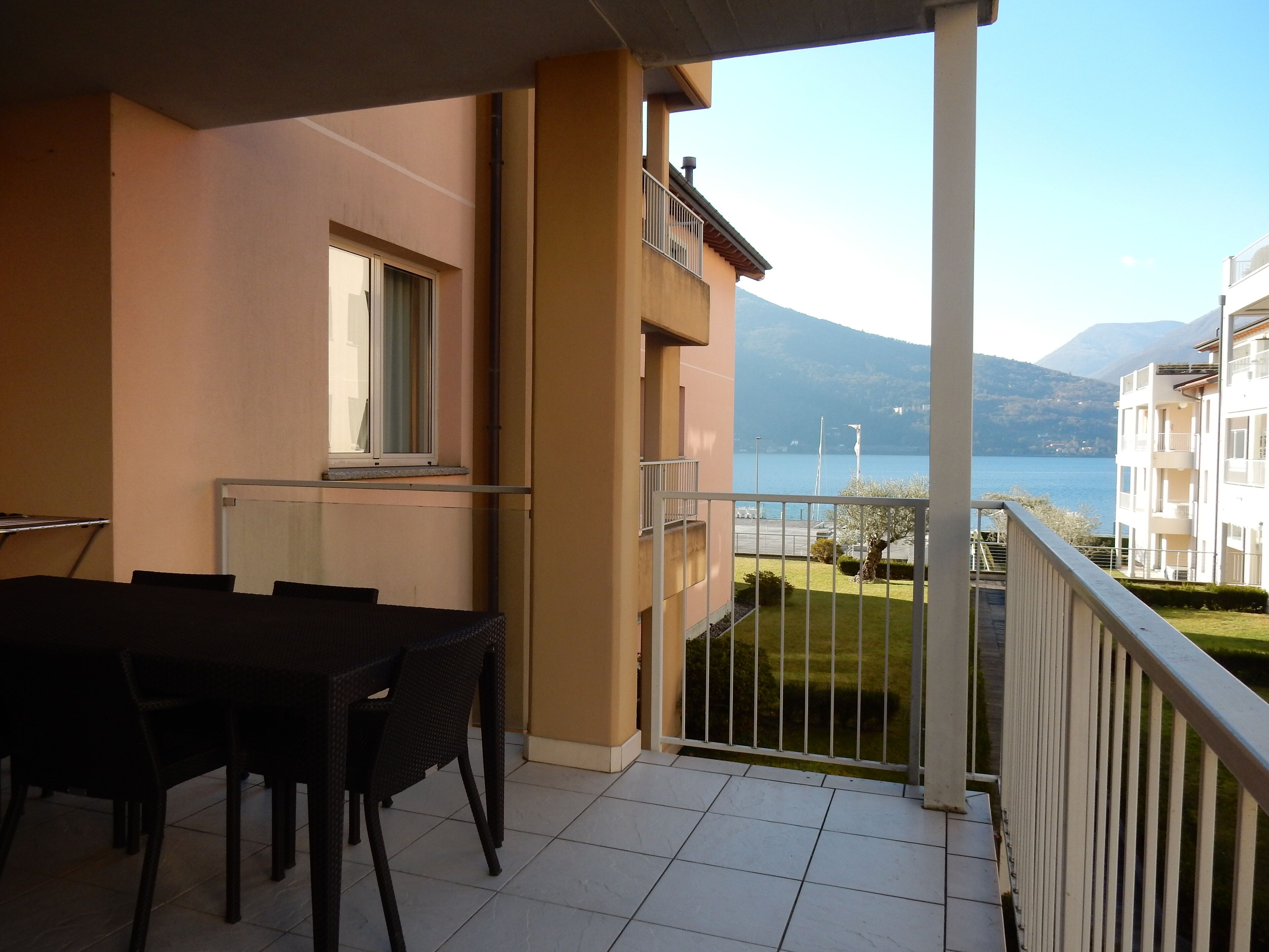 A balcony with a table and chairs, a window, and a view of a lake and mountains.