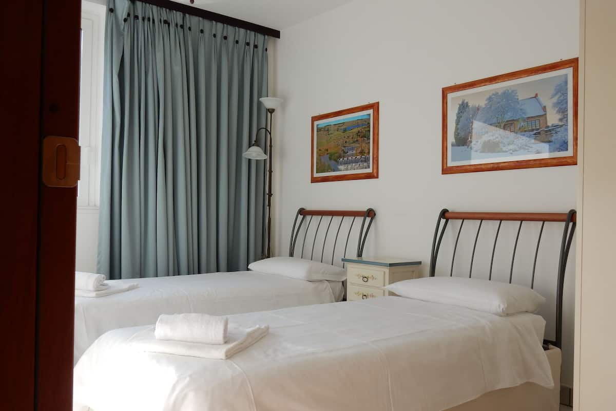 A hotel room with two beds, a nightstand, a lamp, and two framed pictures on the wall.
