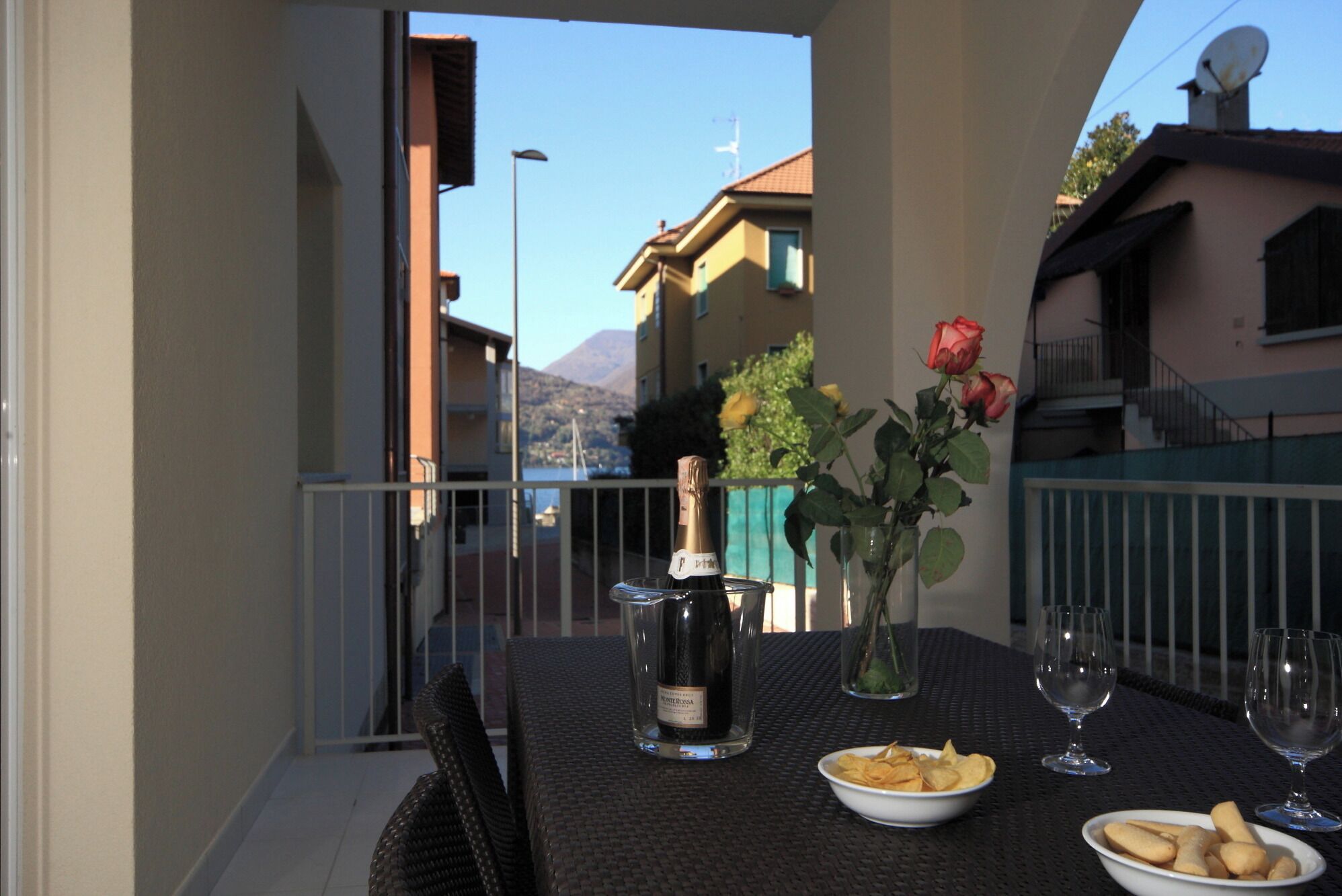 Een balkon tafel met een fles wijn, een vaas met rozen en een schaal chips.