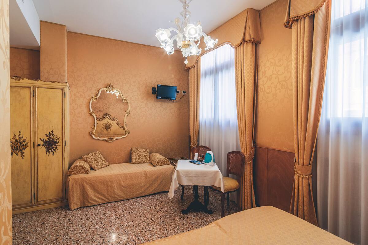Una habitación con una cama, una mesita con una silla, un televisor y un armario.
