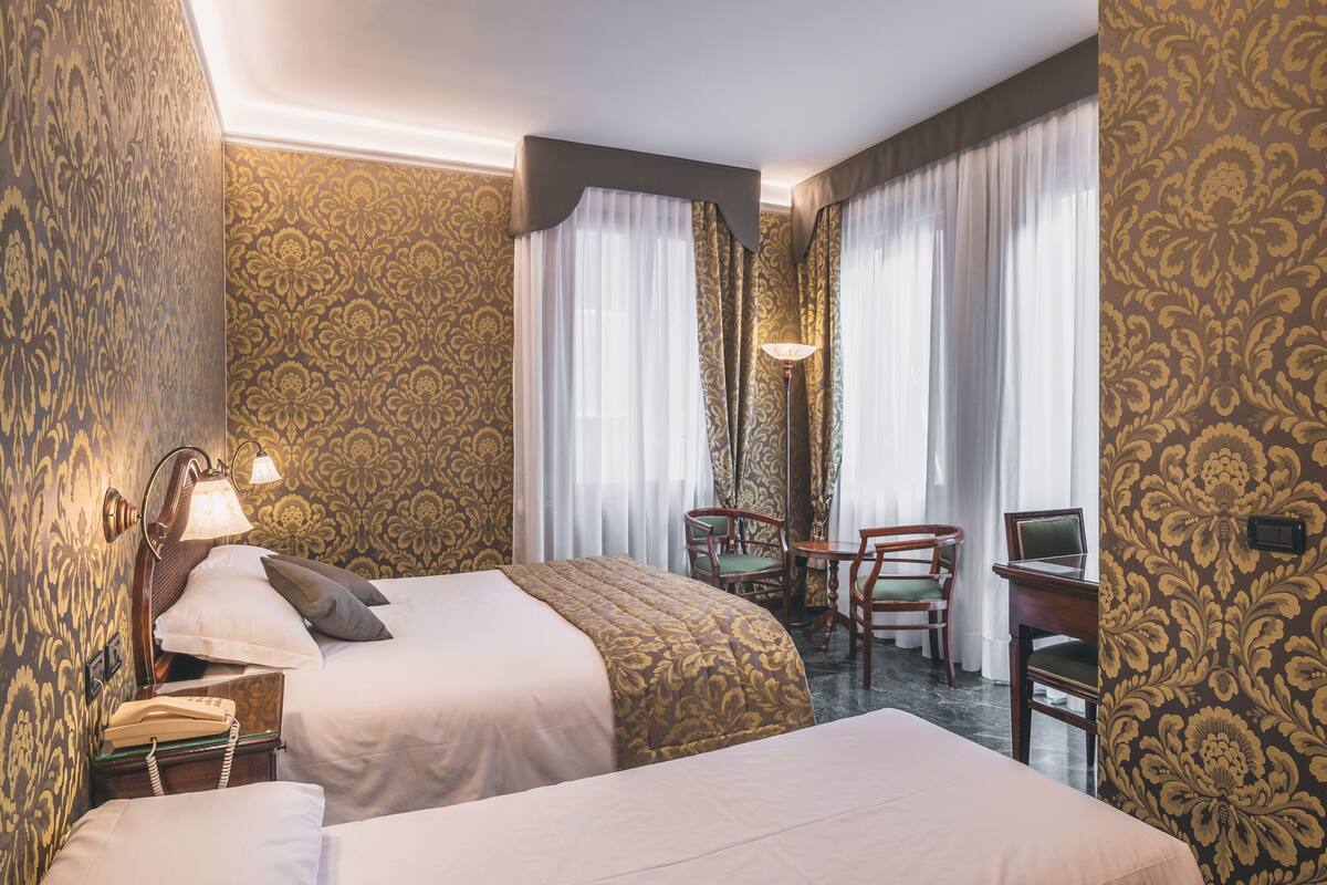 Una habitación de hotel con dos camas, un escritorio con silla, una lámpara y un teléfono.