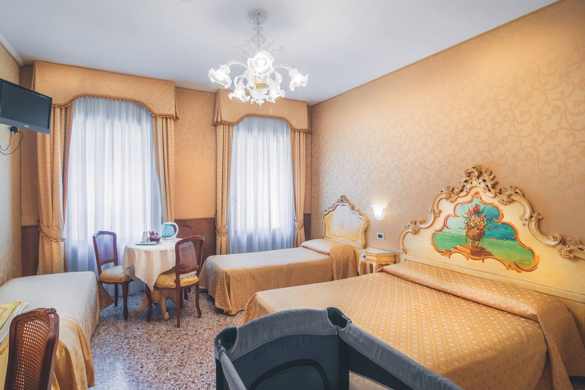 Habitación de hotel con dos camas, una mesita, sillas, televisión y un candelabro.