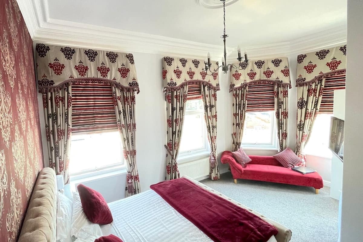 A bedroom with a large bed, a red sofa, and a window with curtains.