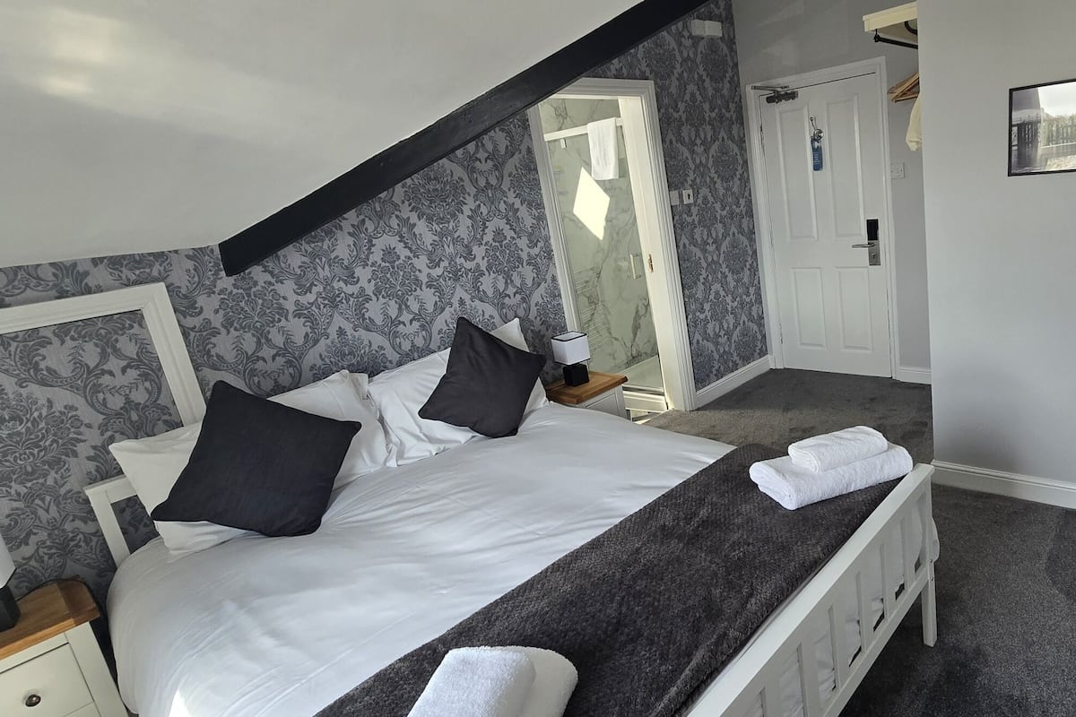 A bedroom with a bed, bedside tables, a nightstand, a lamp, a towel, a picture frame, and a door.