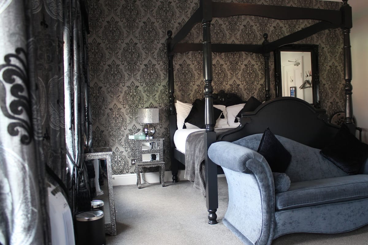 A bedroom with a four-poster bed, a nightstand, a dresser, and a blue armchair.
