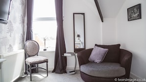 Una habitación con ventana, una silla, un sofá, un espejo y un cuadro en la pared.