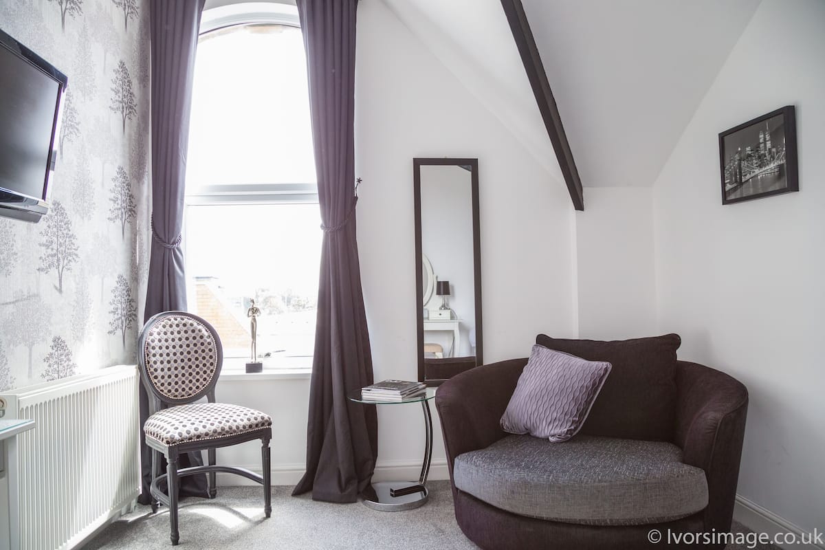 A room with a window, a chair, a sofa, a mirror, and a framed picture on the wall.