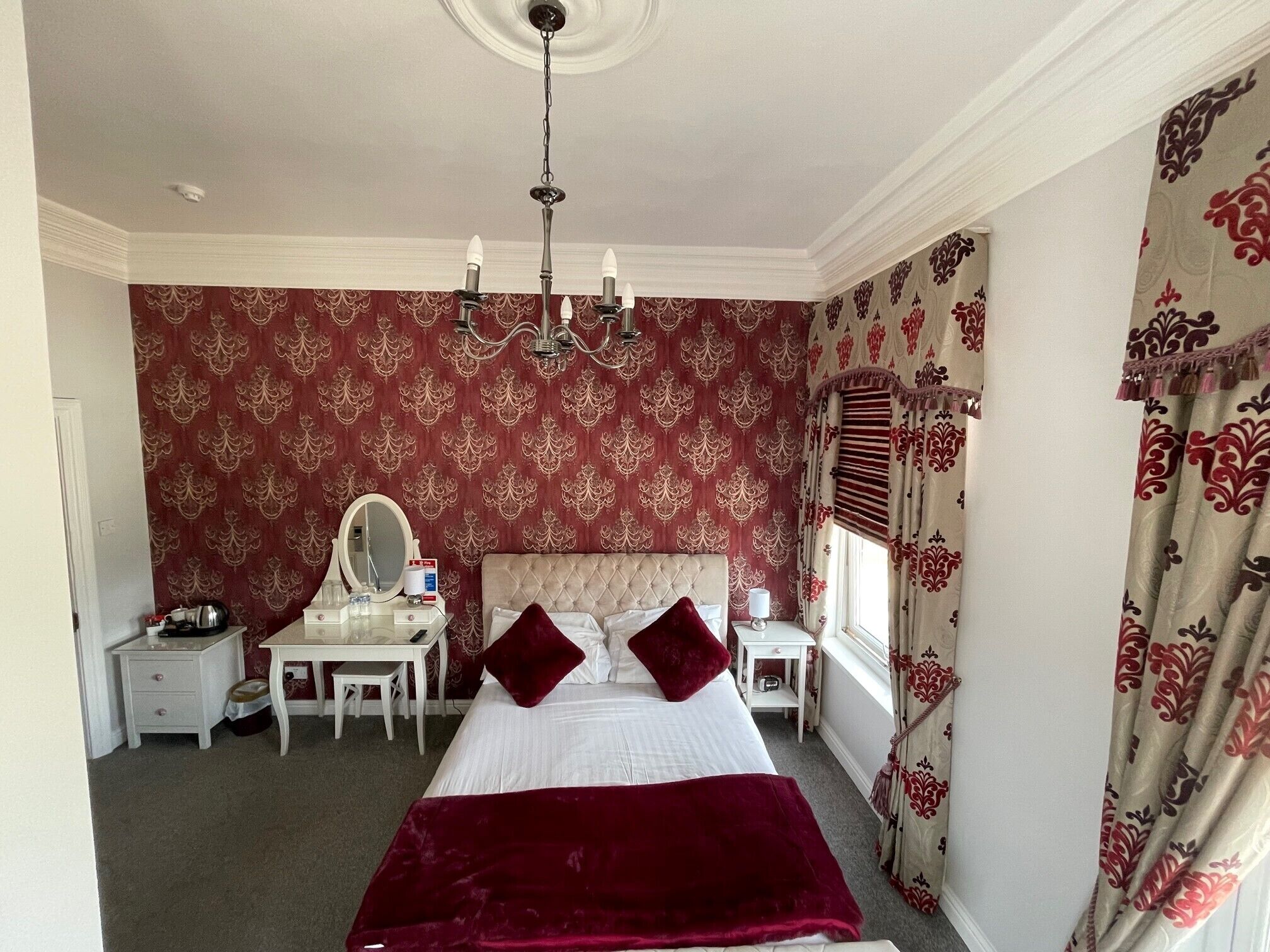 A bedroom with a large bed, a vanity with a mirror, a desk, and a chandelier.