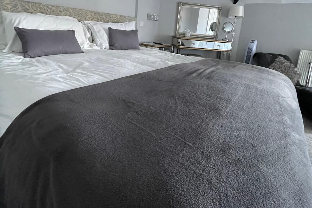 A modern hotel room with a large bed, a bedside table, a mirror, and a dresser.