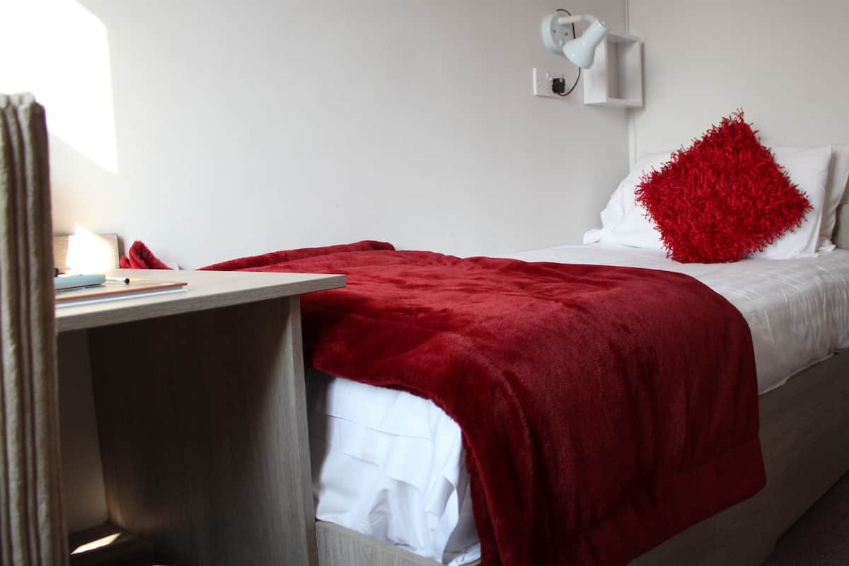 A hotel room with a bed, a desk, and a red throw blanket.