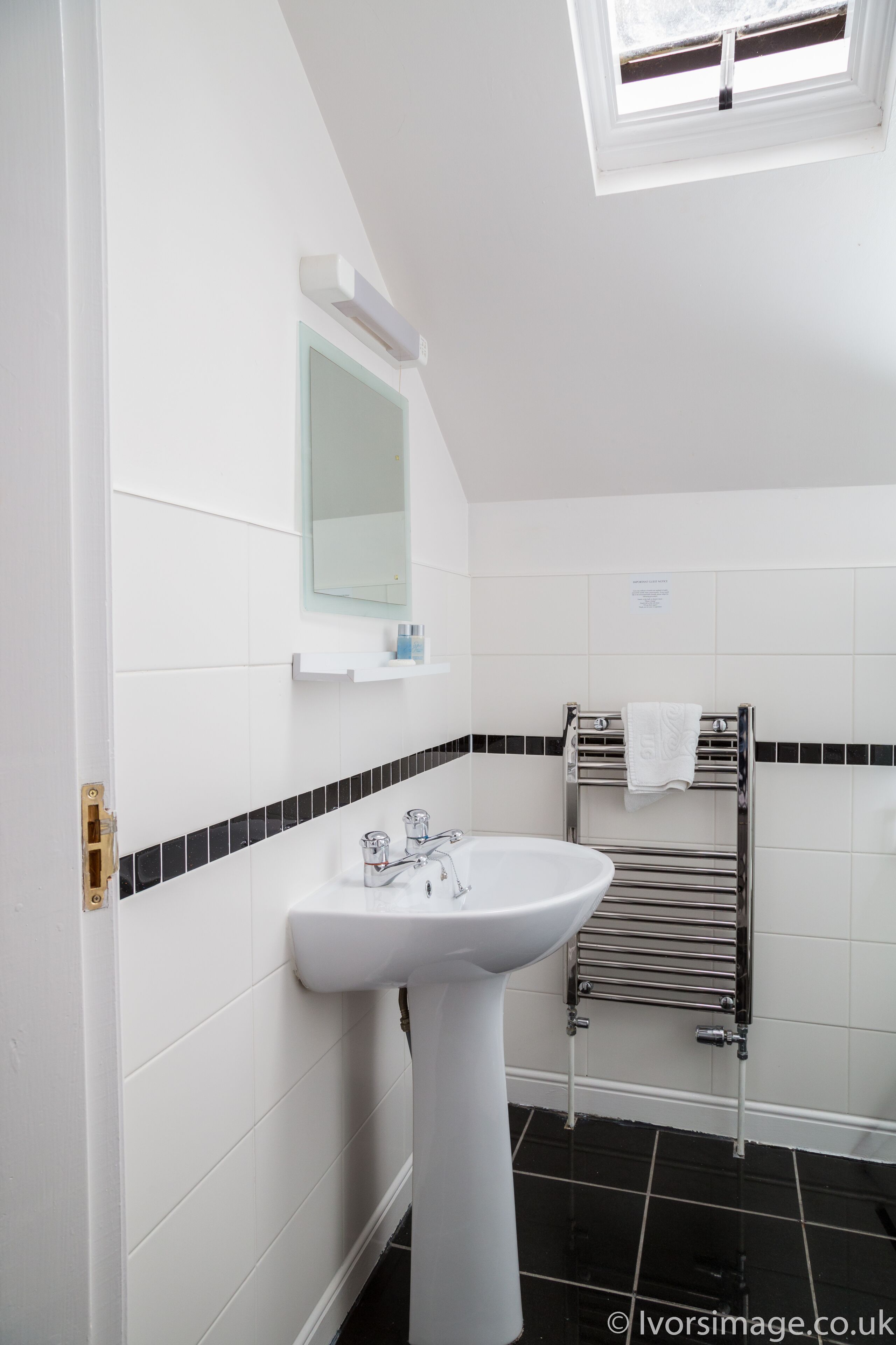 Un baño moderno con lavamanos pedestal, espejo, perchero y ventana.
