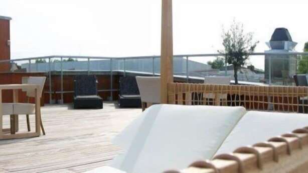 Una terraza con mobiliario exterior y un edificio con un cartel.