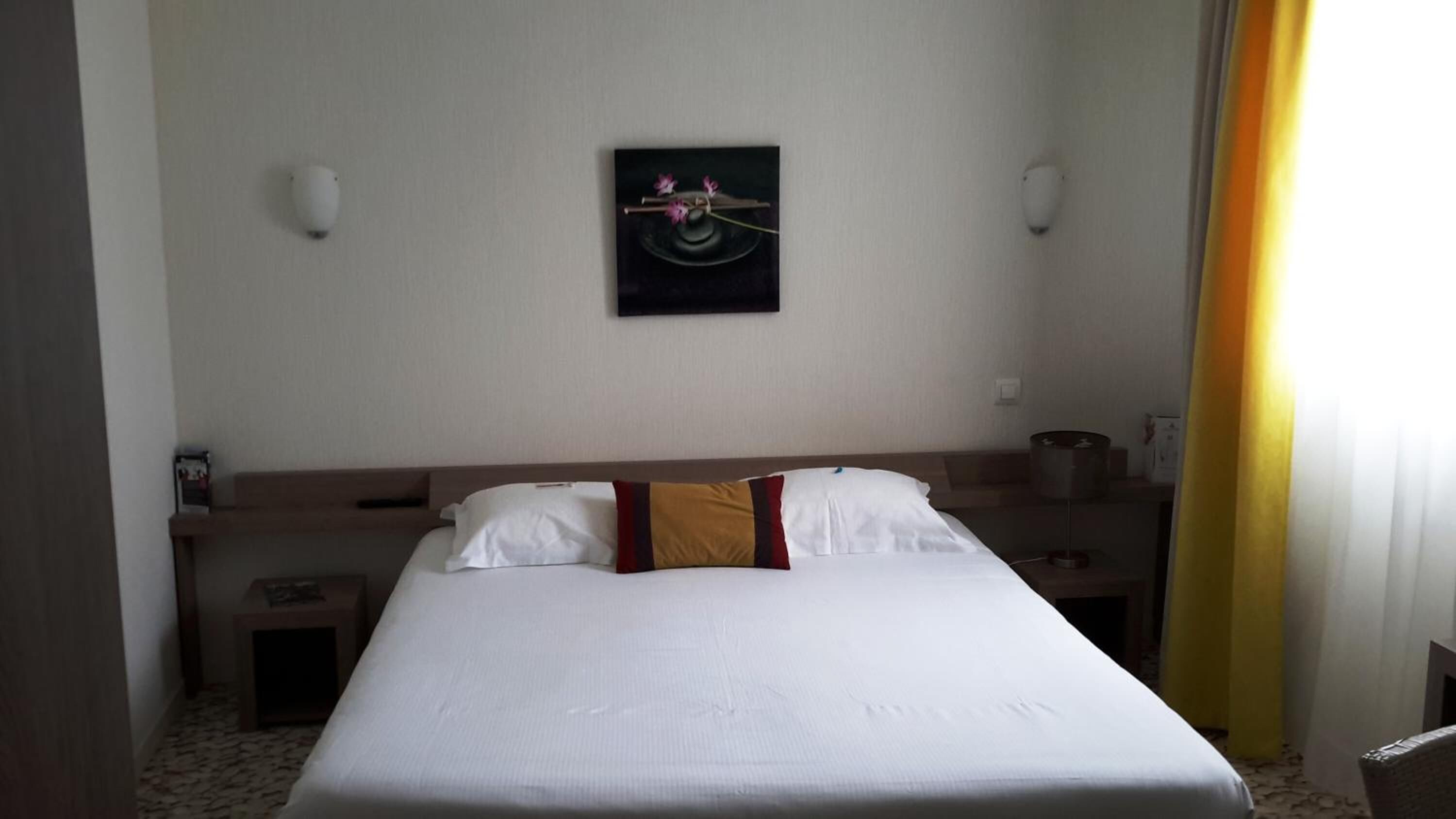 Een hotelkamer met een groot bed, nachtkastje, wanddecoratie en een raam met gordijnen.