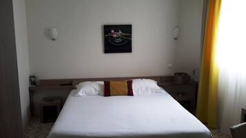 A hotel room with a large bed, a bedside table, a nightstand, a wall-mounted artwork, and a window with curtains.