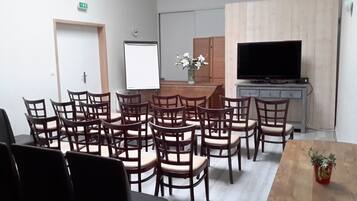 Un salón de conferencias con sillas de madera, una pizarra, un televisor y una pequeña mesa con una planta.