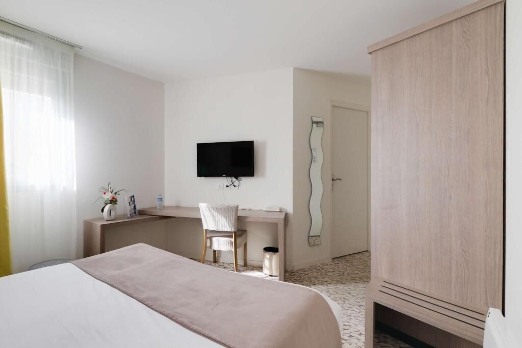 A hotel room with a bed, a desk with a chair, a television, and a wardrobe.
