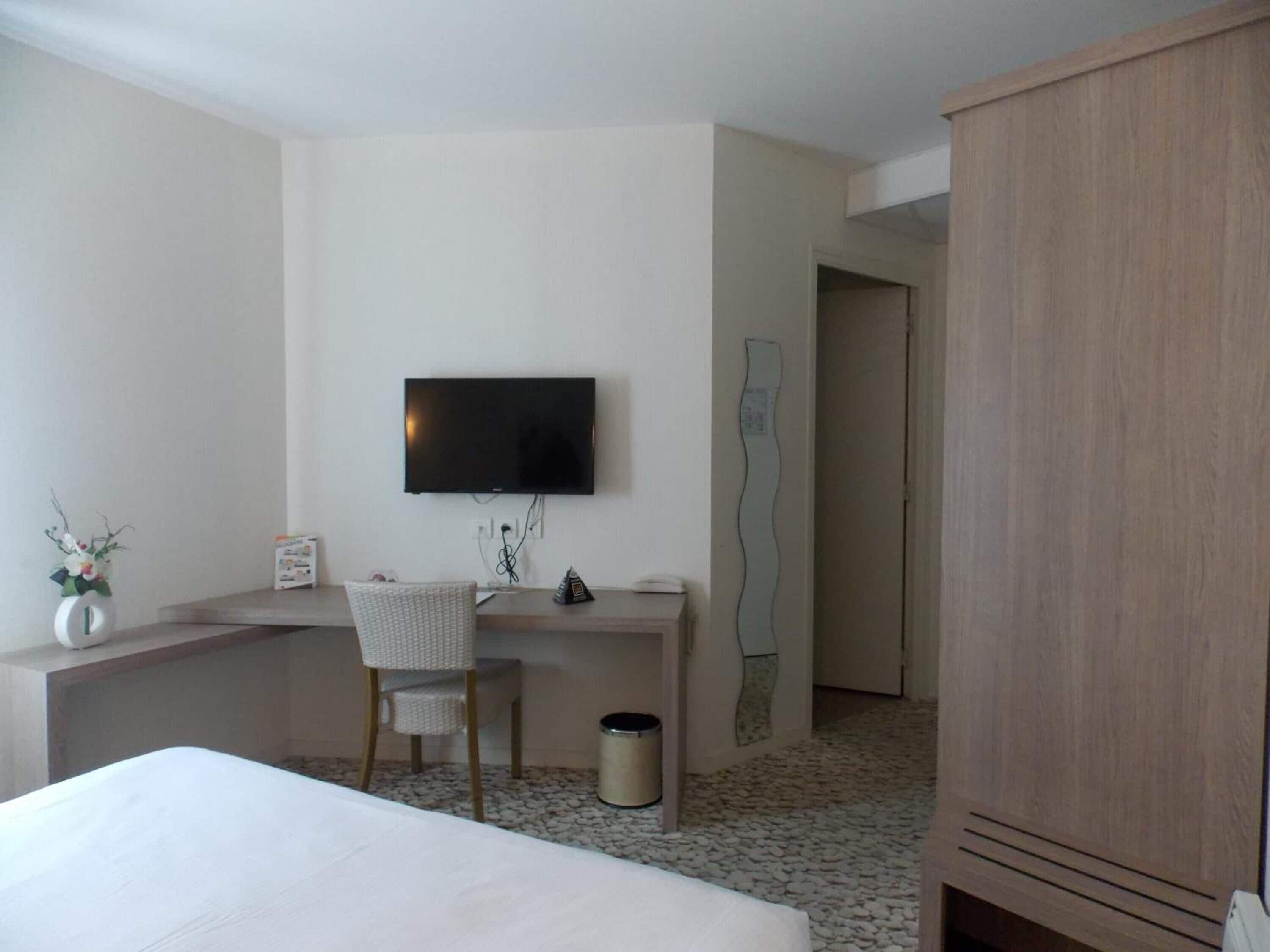 Ein Hotelzimmer mit einem Bett, einem Schreibtisch mit Stuhl, einem Fernseher, einem Mülleimer und einem Kleiderschrank.