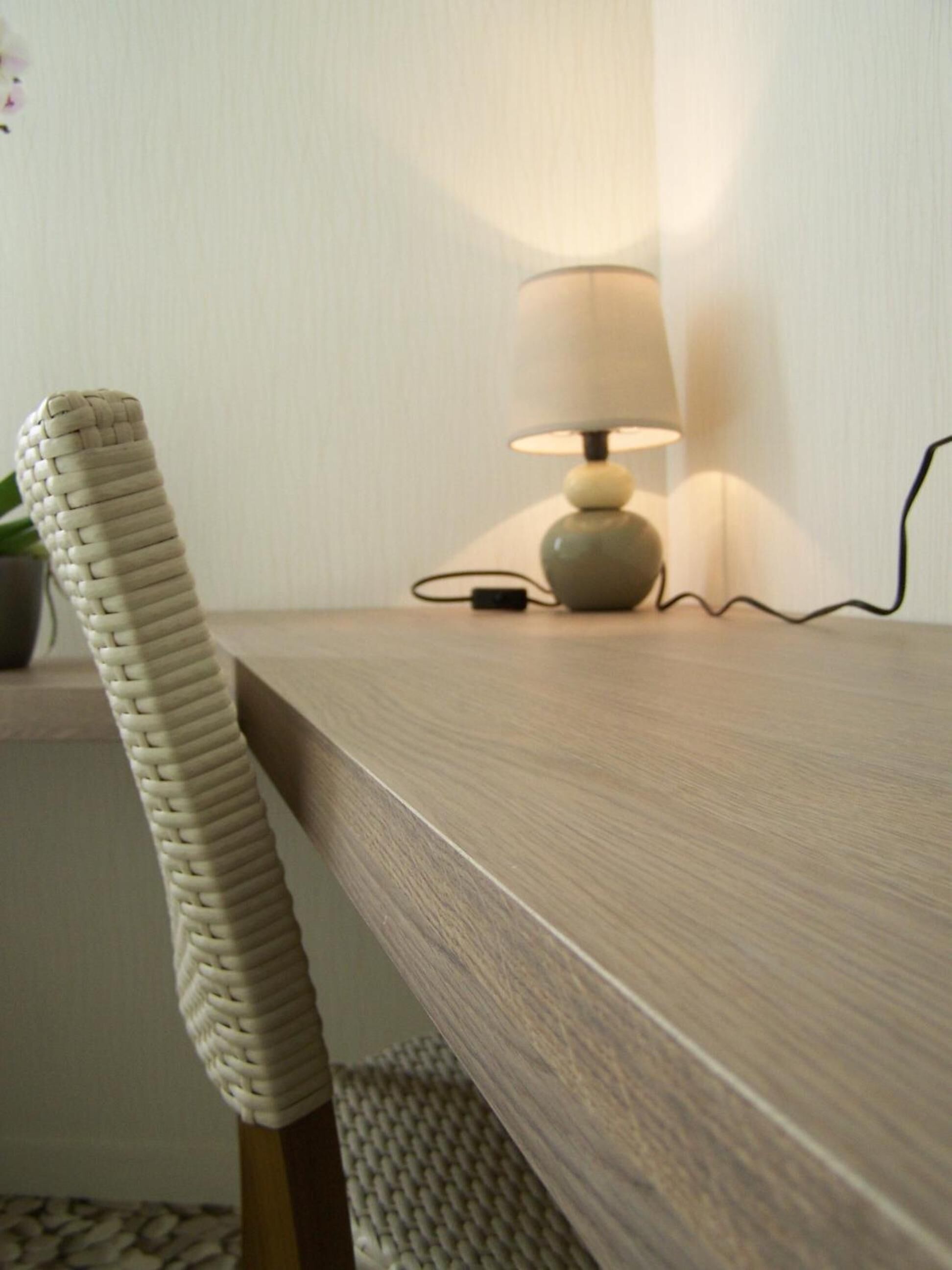 A wooden desk with a lamp and a woven chair.