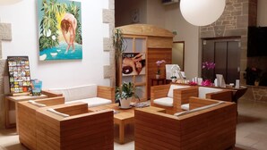 Zona de recepción de un spa con mobiliario de madera, mostrador de recepción y un cartel con una mujer en una piscina.