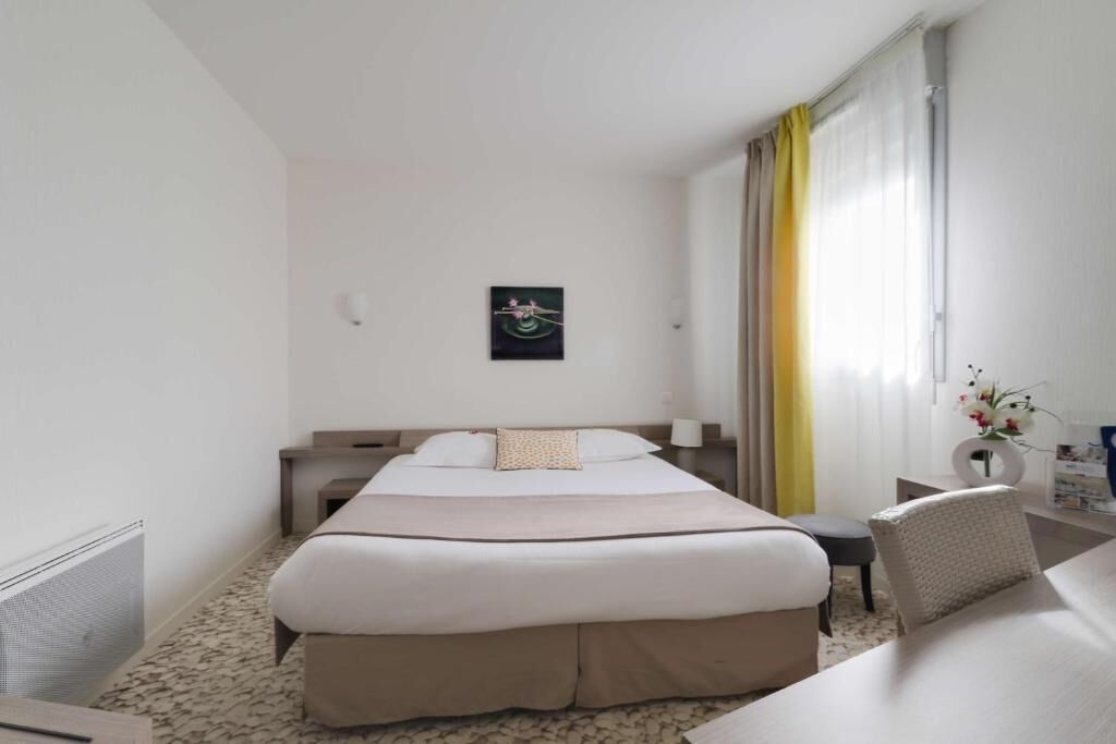 Une chambre d’hôtel comprenant un grand lit, un bureau, une chaise, une table de chevet, une lampe, une fenêtre avec des rideaux et une œuvre d’art accrochée au mur.