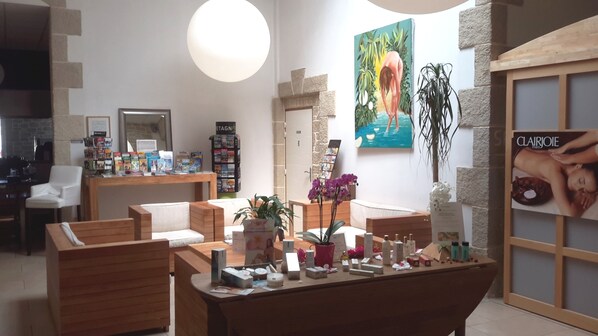 A spa-like setting with wooden furniture, a reception desk, and a poster of a woman in a bathtub. - Brit Hotel Alghotel (Cancale)