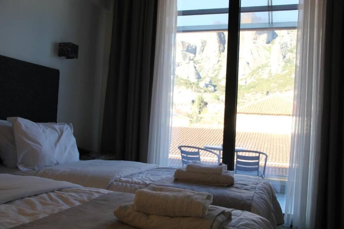 A hotel room with two beds, a large window with a view of rocky terrain, and a chair outside.